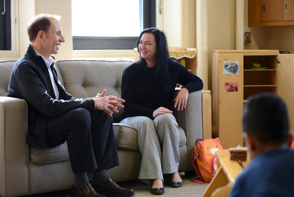 Two smiling adults converse while sitting on a sofa in a preschool classroom