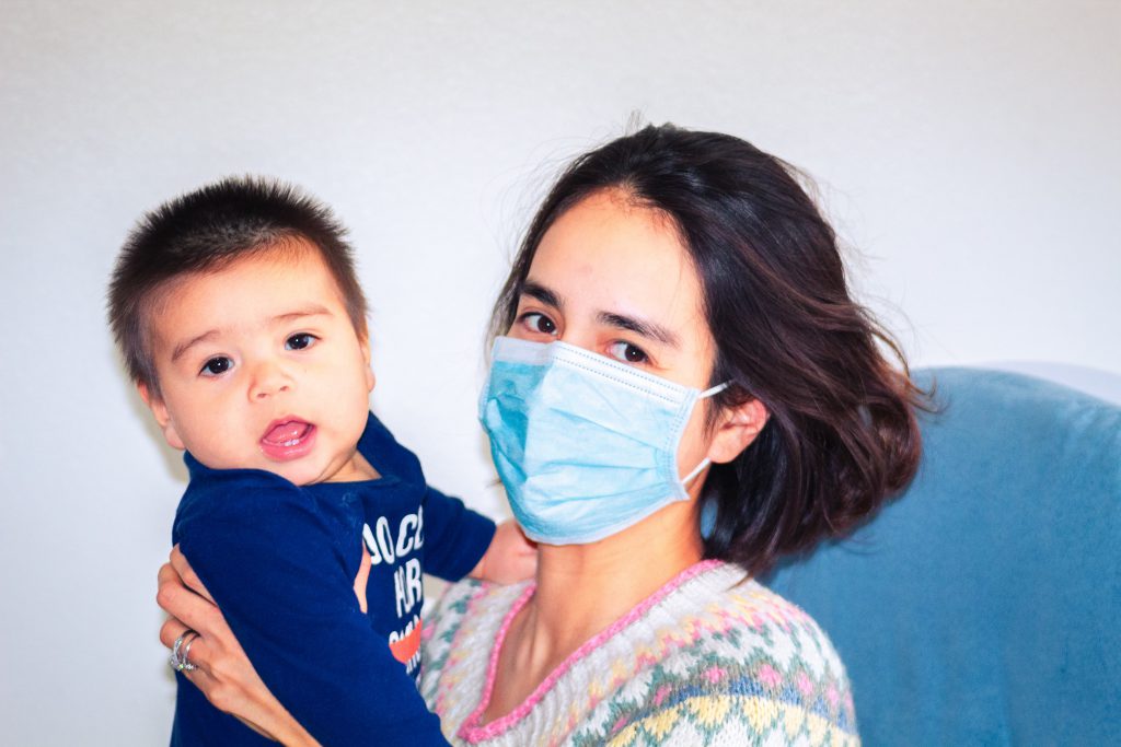 A woman wearing a face mask holds a baby