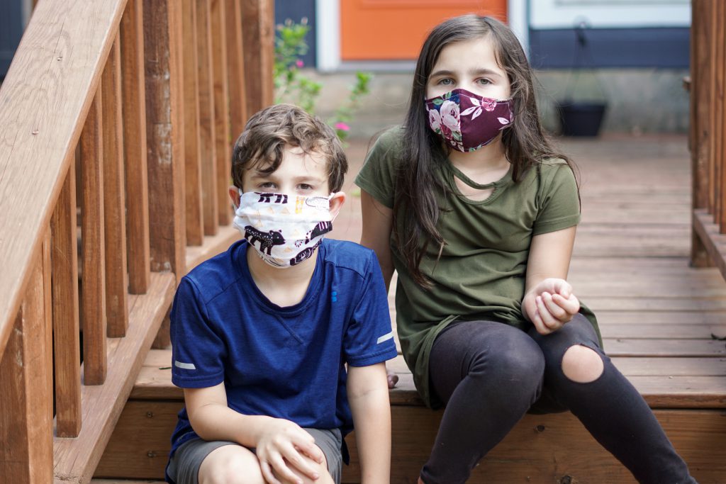 Two children wearing cloth masks sit on stairs