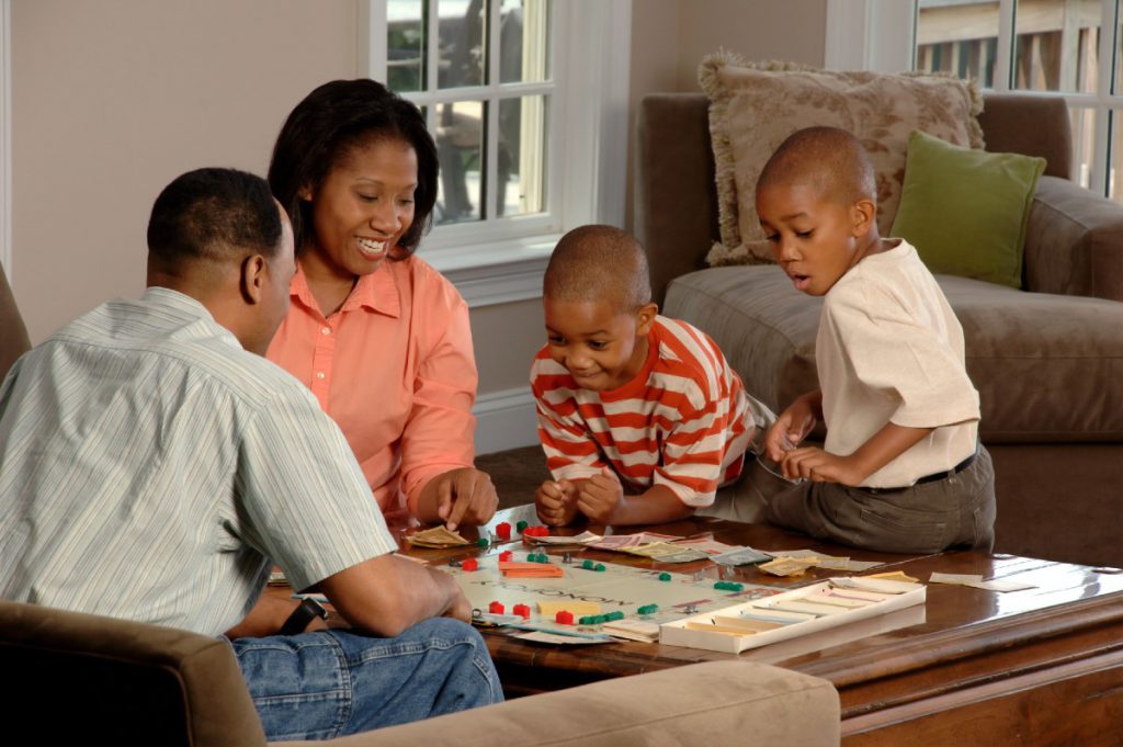 A family of two adults and two young children play Monopoly