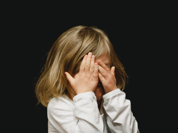 A young child covers her face with her hands.