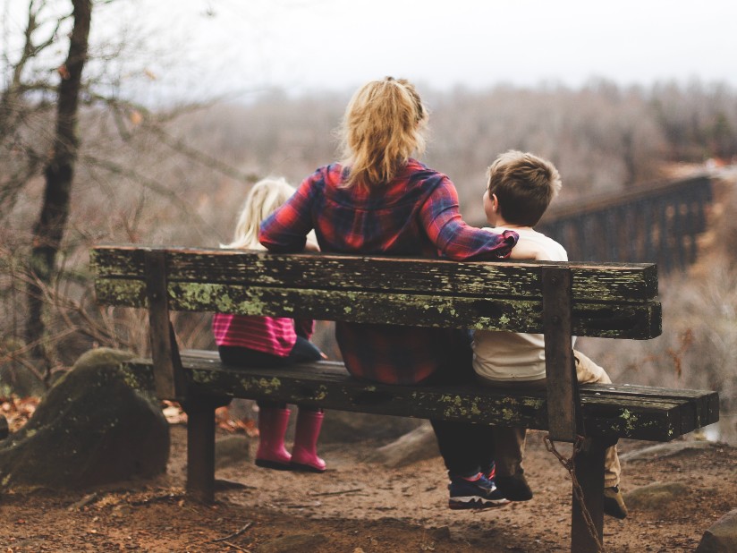 Woman with two children on moss-covered bench overlooking a ravine and  a railroad bridge